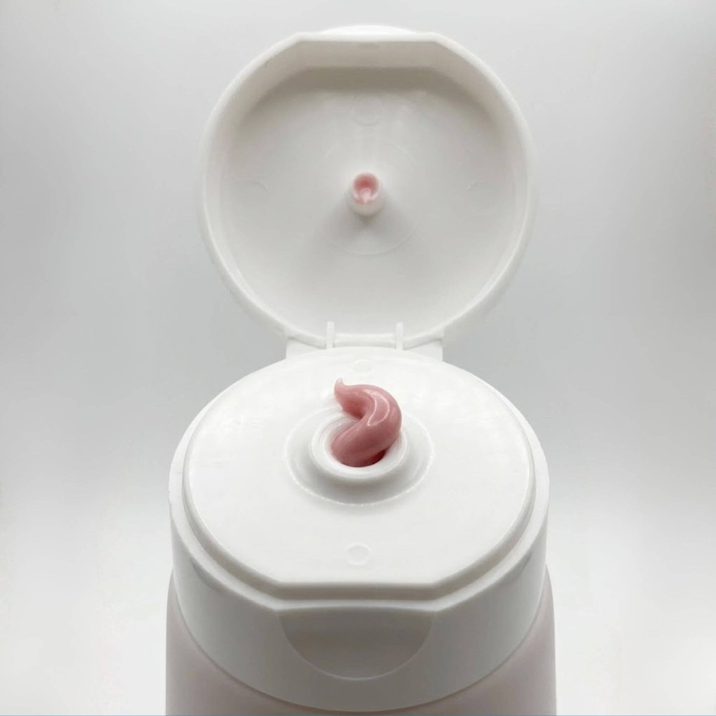 Dettaglio ravvicinato della texture morbida e rosata della crema Claride Fitocosmesi che fuoriesce dall'erogatore di un tubo bianco aperto. Scatto macro che evidenzia la densità e la lucentezza del trattamento.