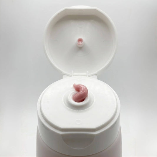 Dettaglio ravvicinato della texture morbida e rosata della crema Claride Fitocosmesi che fuoriesce dall'erogatore di un tubo bianco aperto. Scatto macro che evidenzia la densità e la lucentezza del trattamento.