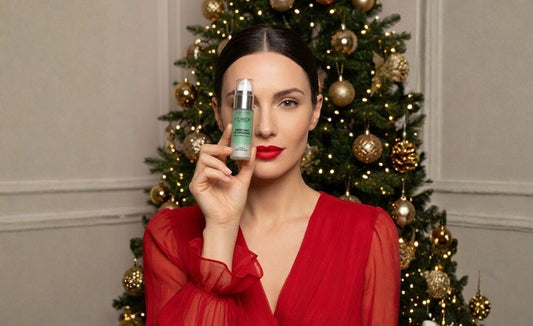 Modella in abito rosso natalizio mostra il Siero Viso ai Liposomi di Claride Fitocosmesi davanti a un albero di Natale illuminato.