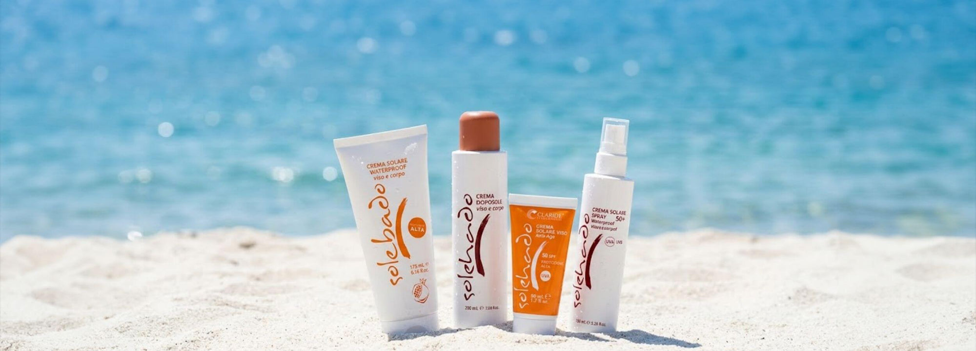 Prodotti solari della linea Solehado di Claride Fitocosmesi adagiati sulla sabbia bianca con mare cristallino sullo sfondo. Banner della Promozione Estiva: 10% di sconto su tutto il catalogo per il mese di Giugno.