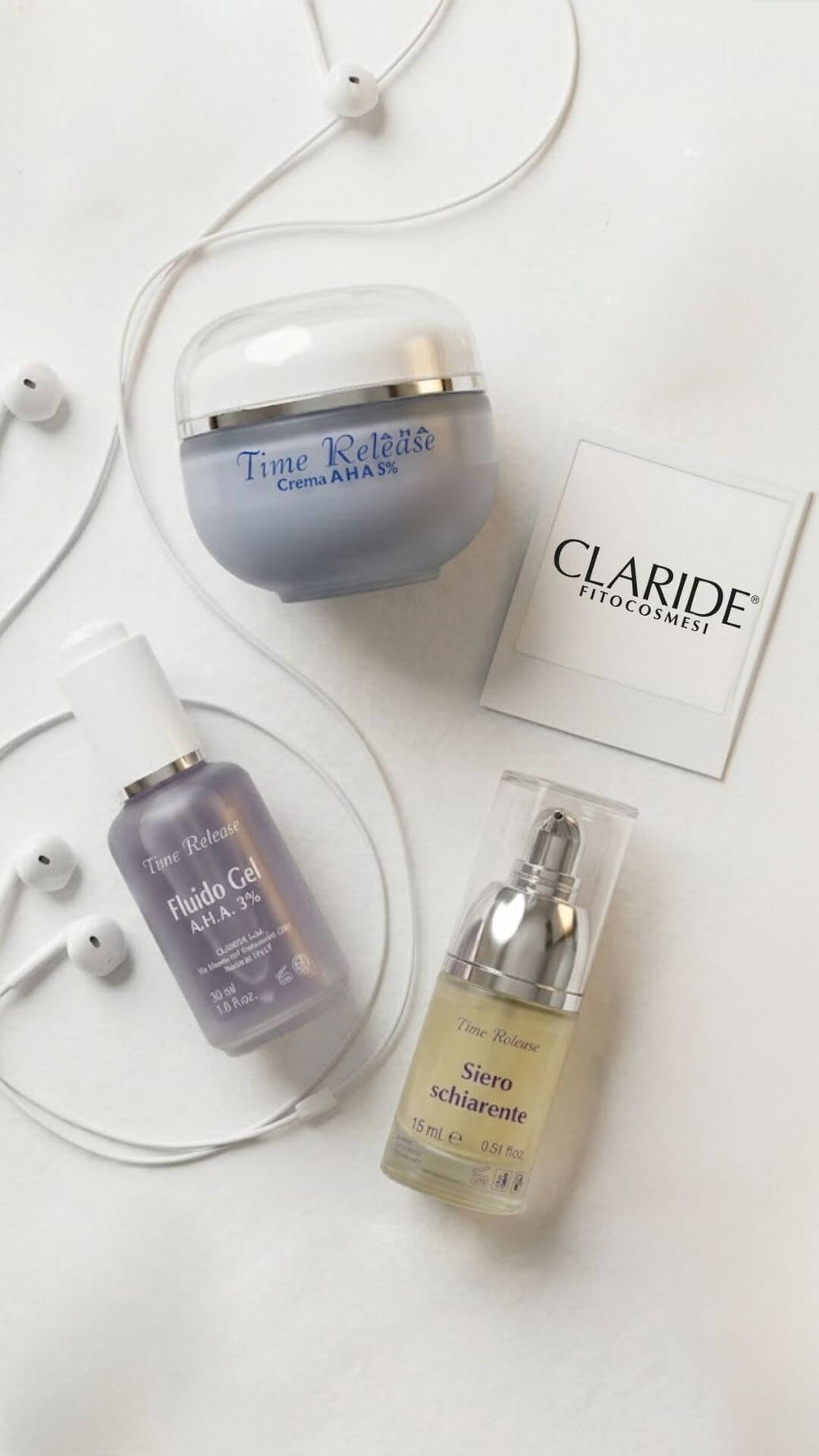Banner mobile della homepage di Claride Fitocosmesi. Composizione lifestyle su marmo bianco con auricolari e i trattamenti viso della linea Time Release: Crema A.H.A. 5%, Fluido Gel A.H.A. 3% e Siero Schiarente.