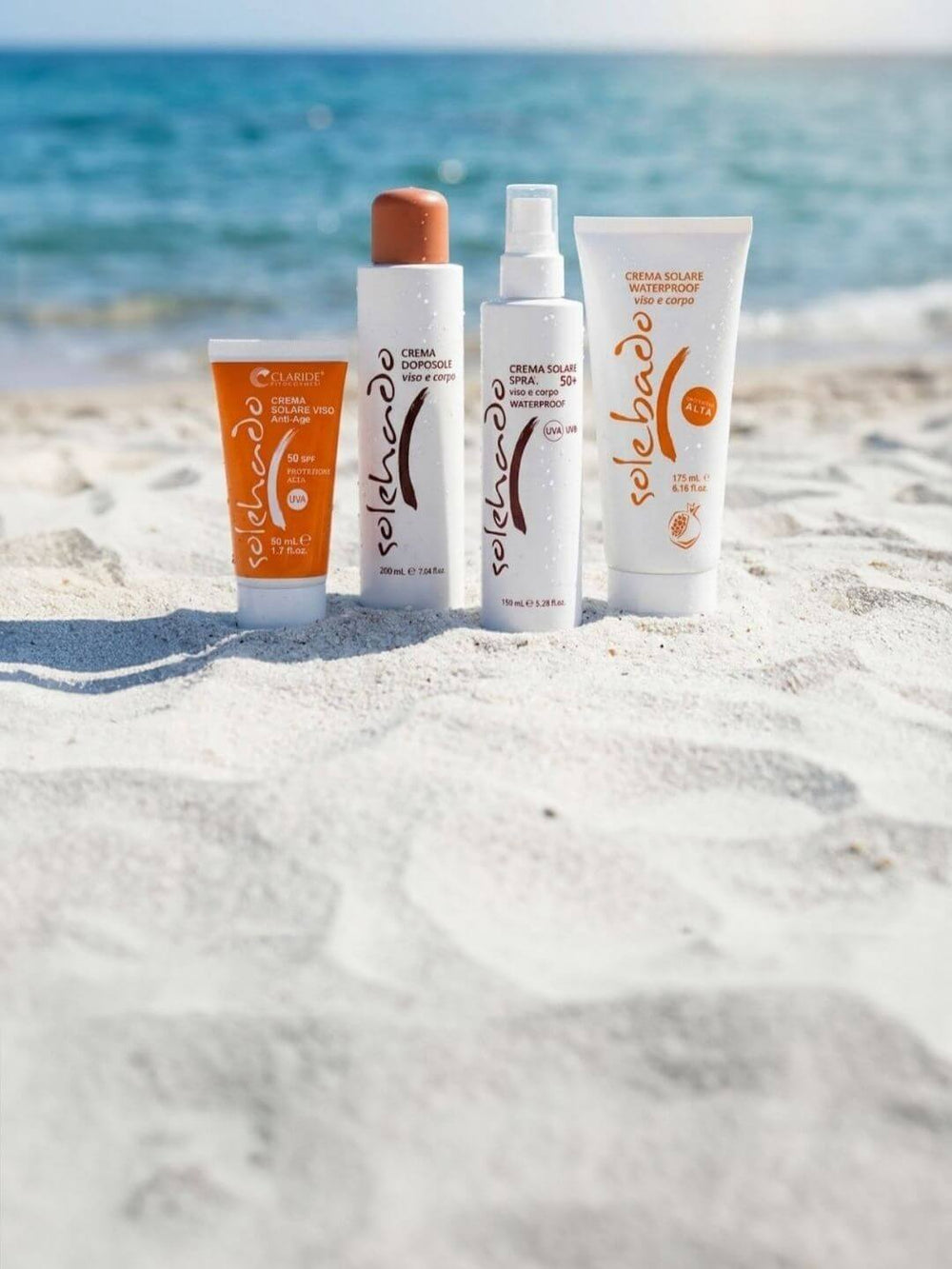 Prodotti solari della linea Solehado di Claride Fitocosmesi adagiati sulla sabbia bianca con mare cristallino sullo sfondo. Banner della Promozione Estiva: 10% di sconto su tutto il catalogo per il mese di Giugno.