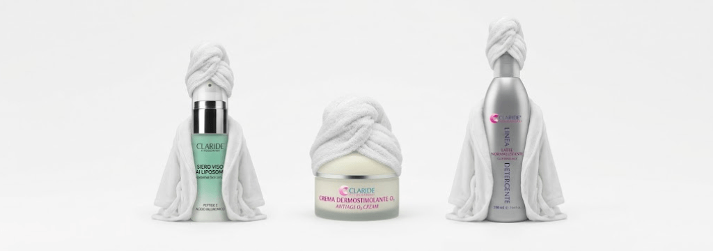 Siero viso ai liposomi, crema dermostimolante O2 e latte normalizzante Claride con asciugamano spa a turbante su sfondo bianco