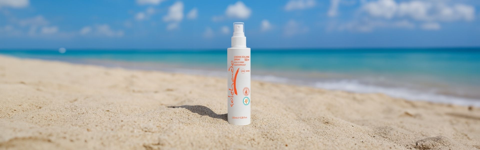 Crema solare spray SPF 50+ ad alta protezione, resistente all'acqua, posizionata sulla sabbia di una spiaggia tropicale.