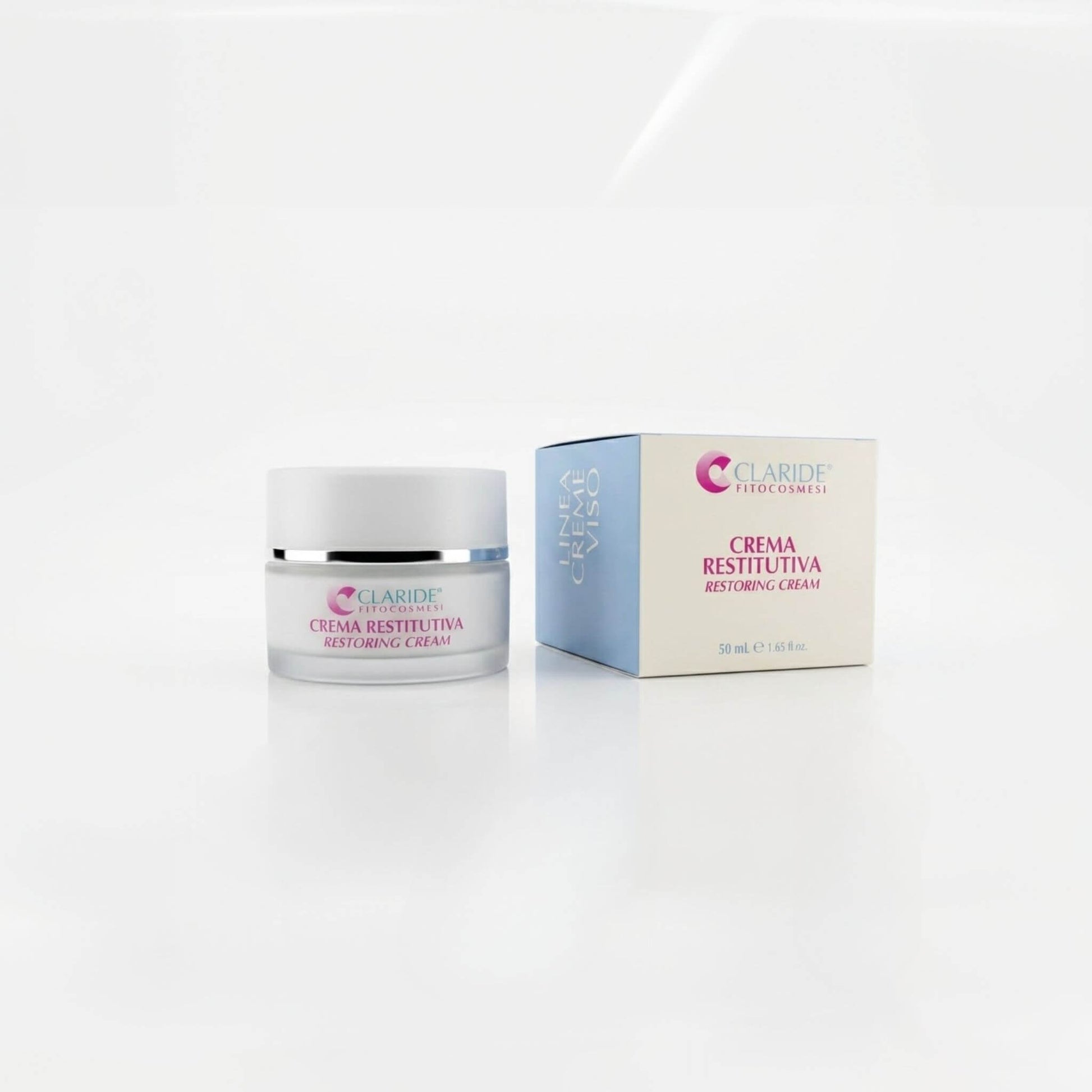 Vasetto in vetro satinato e scatola azzurra e panna della Crema Restitutiva Claride Fitocosmesi. Trattamento viso riparatore e nutriente (Restoring Cream) per restituire compattezza alla pelle stanca e stressata, su fondo bianco con riflesso.