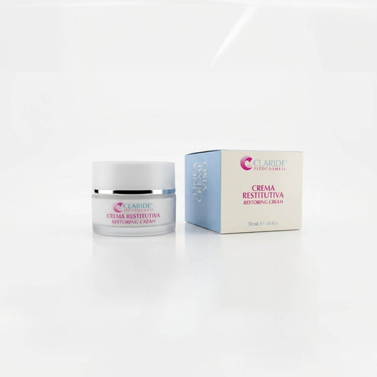 Vasetto in vetro satinato e scatola azzurra e panna della Crema Restitutiva Claride Fitocosmesi. Trattamento viso riparatore e nutriente (Restoring Cream) per restituire compattezza alla pelle stanca e stressata, su fondo bianco con riflesso.