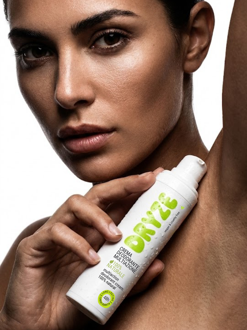 Modella che mostra il flacone di crema deodorante Dryze multiazione 100% naturale e vegan vicino all'ascella su sfondo bianco.