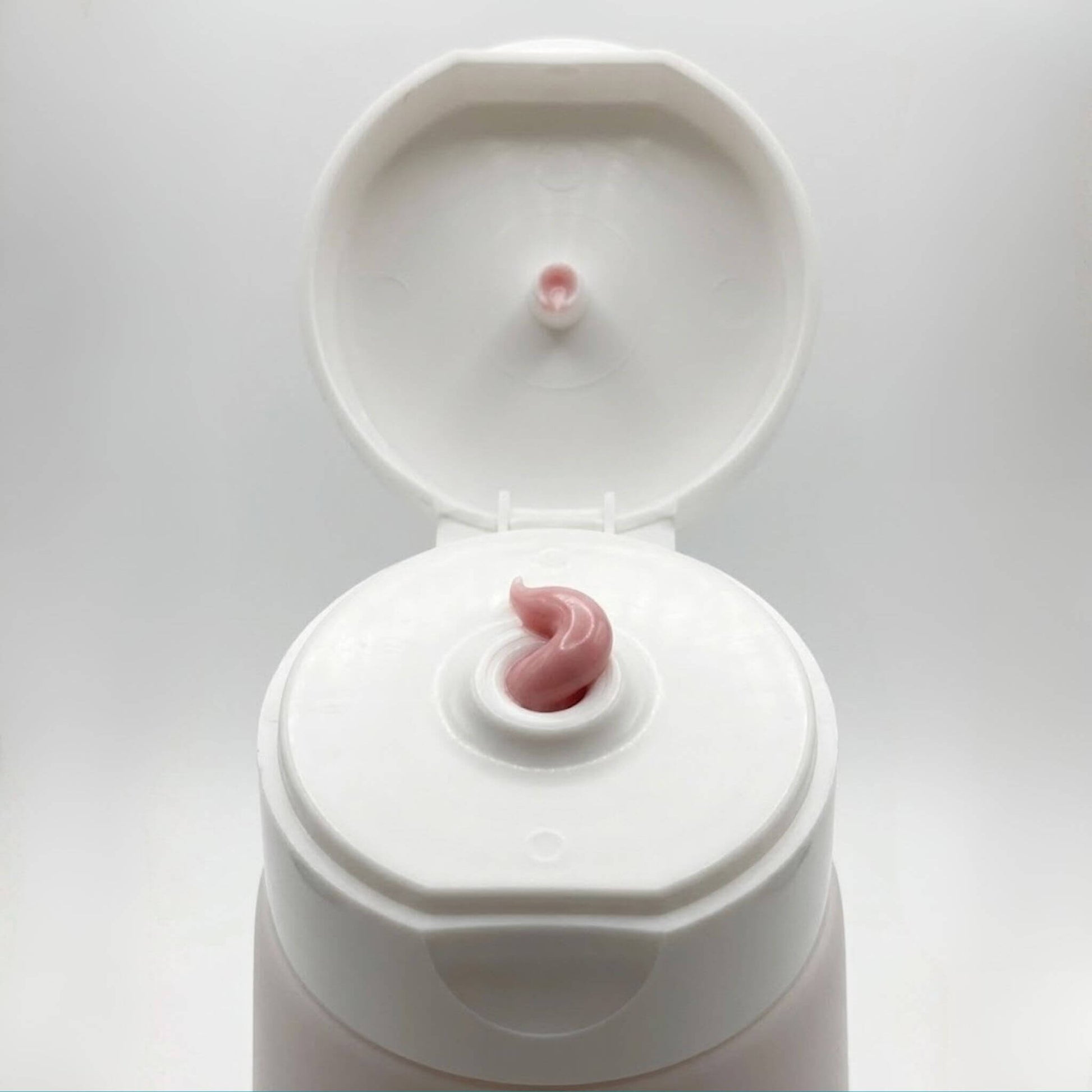 Dettaglio ravvicinato della texture morbida e rosata della crema Claride Fitocosmesi che fuoriesce dall'erogatore di un tubo bianco aperto. Scatto macro che evidenzia la densità e la lucentezza del trattamento.