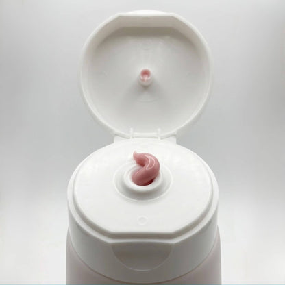 Dettaglio ravvicinato della texture morbida e rosata della crema Claride Fitocosmesi che fuoriesce dall'erogatore di un tubo bianco aperto. Scatto macro che evidenzia la densità e la lucentezza del trattamento.