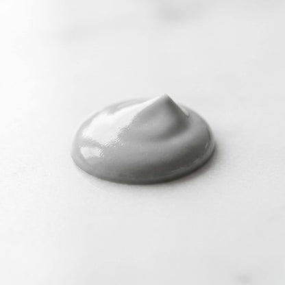 Dettaglio macro della texture cremosa e lucida del deodorante naturale DRYZE di Claride Fitocosmesi. Una goccia densa di color grigio perla che evidenzia la consistenza vellutata e ricca del prodotto, su fondo chiaro.